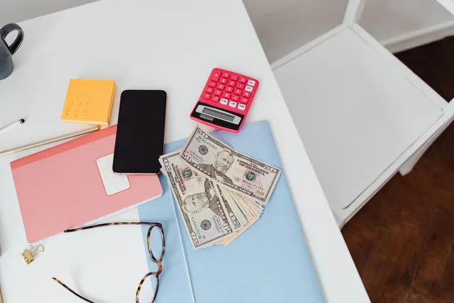 Overhead view of office desk with calculator, money, and glasses, depicting finance and budgeting. Airbnb and Vrbo host fees for Canadian hosts with a CAD 40,000 example